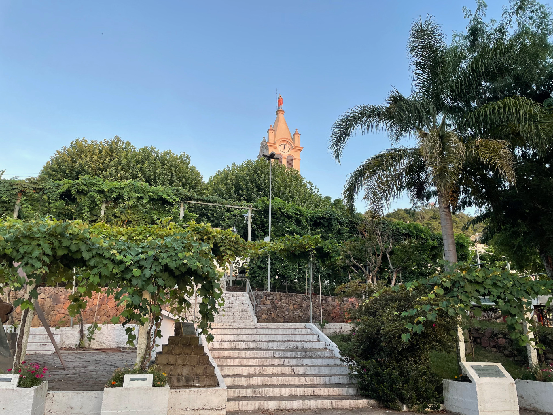 Picture of a staircase surrounded by vineyards. In the background, a church tower and the blue sky.